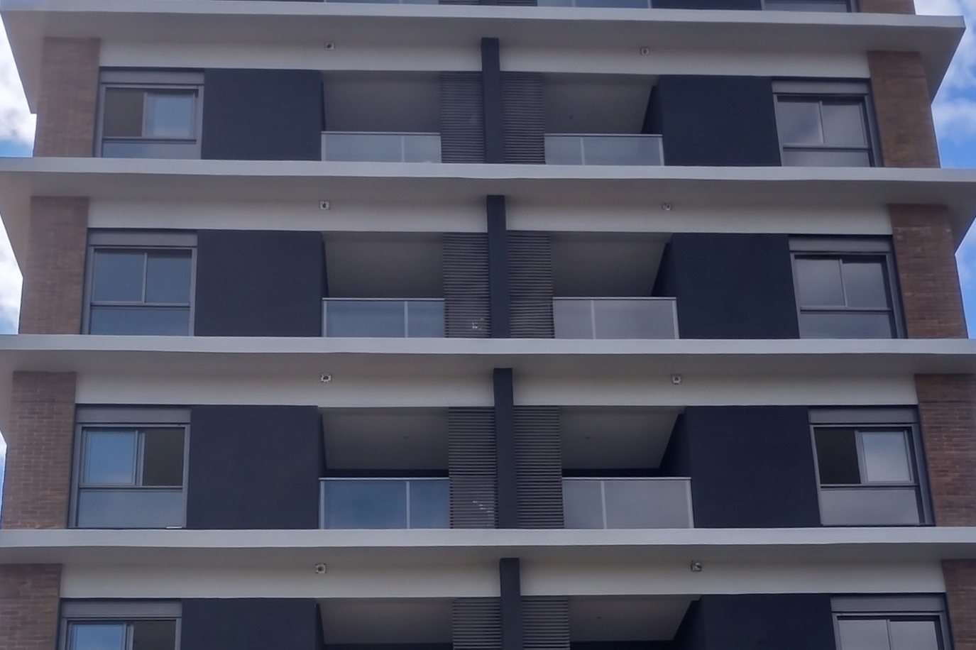 Residencial concluído com fachada em tijolo aparente, pano escuro e lajes brancas